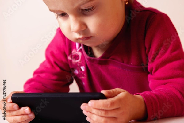 Fototapeta Child smiling brightly in a close-up portrait with her gadget.