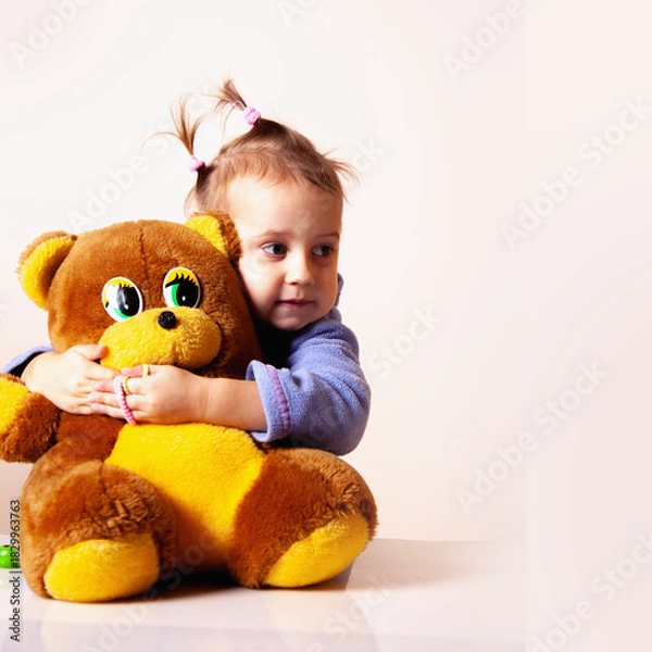 Fototapeta Smiling child holding a soft teddy bear while posing for a playful portrait.