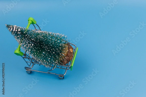 Obraz Shopping cart with Christmas tree on pastel blue background. Christmas shopping concept