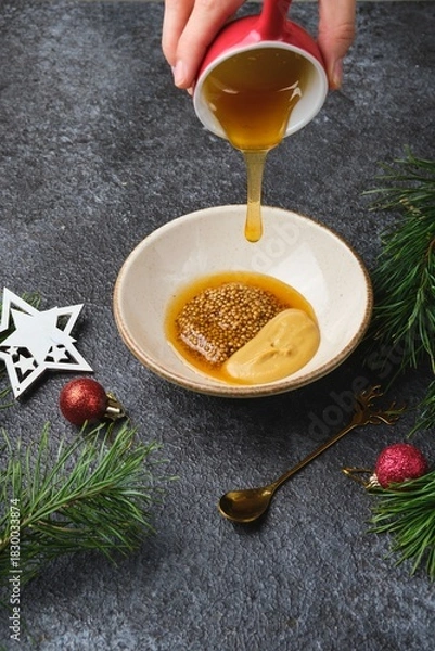Fototapeta Mixing grainy and Dijon mustard with honey for a glaze on roast beef or other meats against a dark background in Christmas decor.