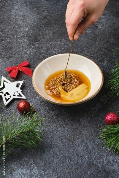 Fototapeta Mixing grainy and Dijon mustard with honey for a glaze on roast beef or other meats against a dark background in Christmas decor.
