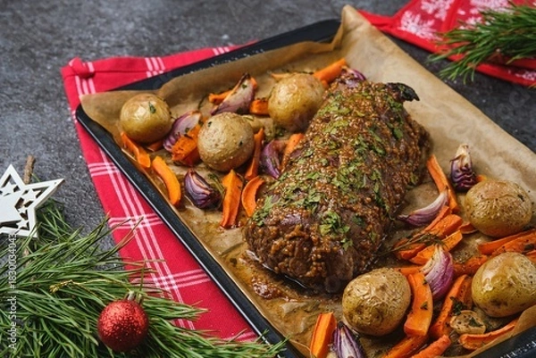 Fototapeta A roast beef loin on a baking sheet with carrots, onions, and potatoes. Cooking beef in the oven as a whole piece. Merry Christmas.