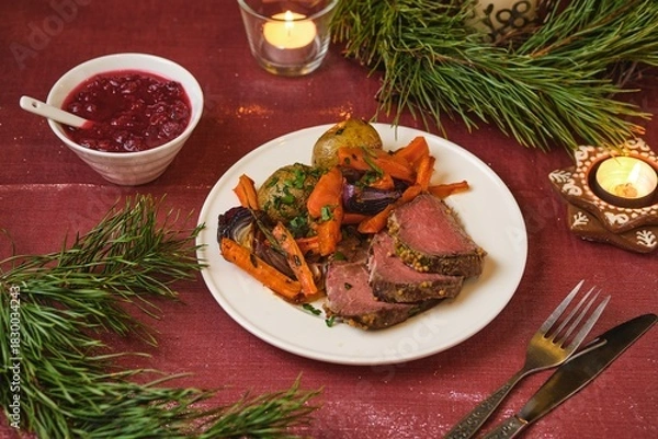 Fototapeta A serving of roast beef with potatoes, carrots, and onions on a white plate on a festive Christmas table setting. Merry Christmas! Beef dishes.