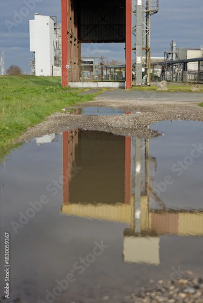 Obraz Réflexion d’une structure industrielle dans une flaque d’eau sur un chemin