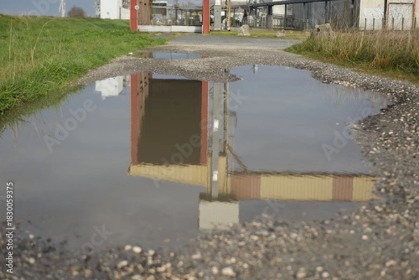 Obraz Reflet d’une structure industrielle dans une flaque d’eau sur chemin en gravier