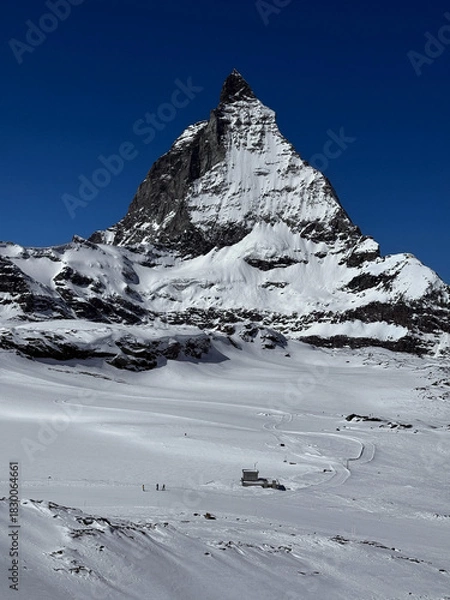 Fototapeta Winter view of the iconic Matterhorn peak covered in snow under a clear blue sky in the Swiss Alps. High-resolution mountain landscape ideal for travel, nature and winter sports themes.