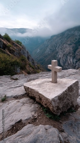 Obraz A small cross carved into a rocky cliff, surrounded by misty mountains at dawn. 