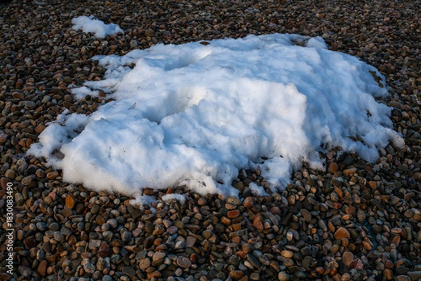 Obraz Patch of melting snow lying on a bed of smooth pebbles, creating a natural contrast of textures in winter light