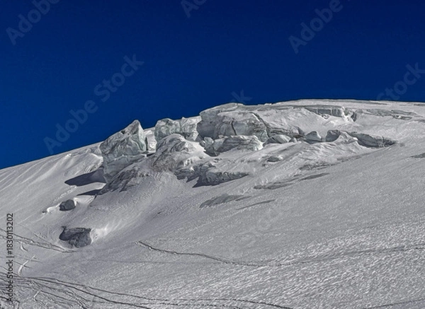 Fototapeta Rocky alpine ridge surrounded by fresh winter snow under a clear deep blue sky. High-altitude landscape of the Swiss Alps with dramatic textures and untouched terrain.