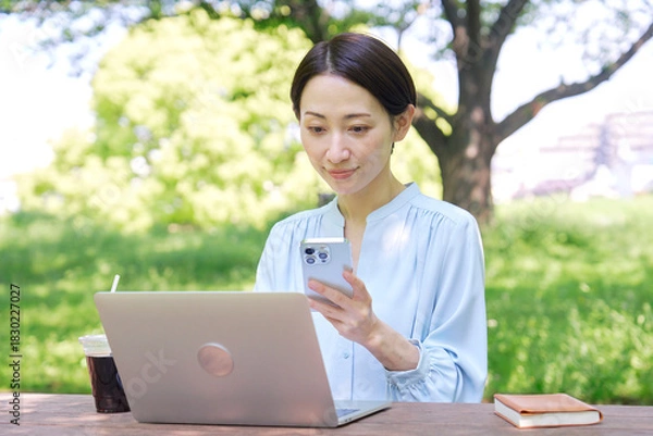 Obraz 屋外でスマートフォンとノートパソコンを使う女性