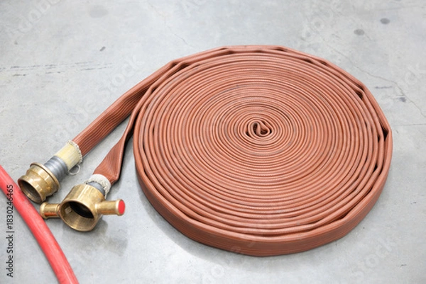 Obraz Coiled brown fire hose with brass coupling on concrete floor