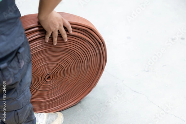 Obraz Worker's hand moving large coiled fire hose on concrete floor
