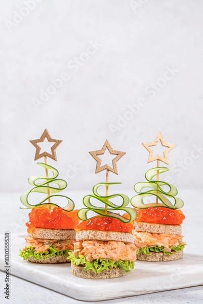 Obraz Creative holiday-themed finger sandwiches shaped like Christmas trees with salmon, cucumber, and lettuce on a serving platter