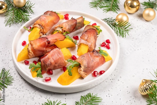 Fototapeta Delicious prosciutto and mango bites topped with arugula and pomegranate on a festive plate