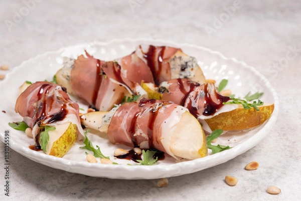 Fototapeta Fresh pear and prosciutto bites served on a white plate with balsamic glaze and pine nuts