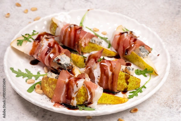 Fototapeta Fresh pear and prosciutto bites served on a white plate with balsamic glaze and pine nuts