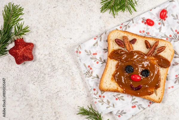 Fototapeta Creative holiday toast with peanut butter and toppings shaped like a reindeer on a festive napkin