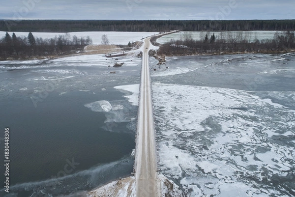 Fototapeta Aerial view of a wooden bridge over a freezing river with ice