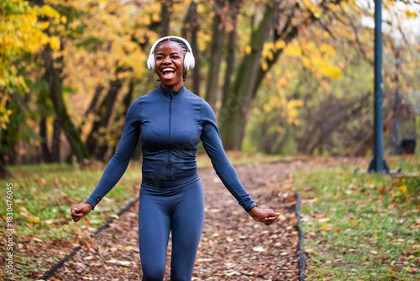 Fototapeta Ecstatic jogger runs on running trail of fallen leaves, with golden and green trees creating a serene, seasonal backdrop.
