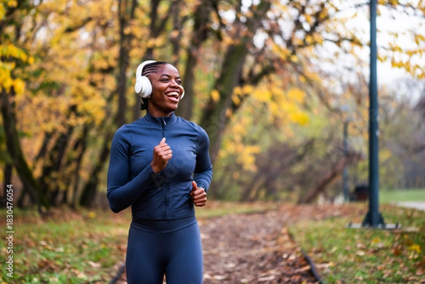 Fototapeta Ecstatic jogger runs on running trail of fallen leaves, with golden and green trees creating a serene, seasonal backdrop.