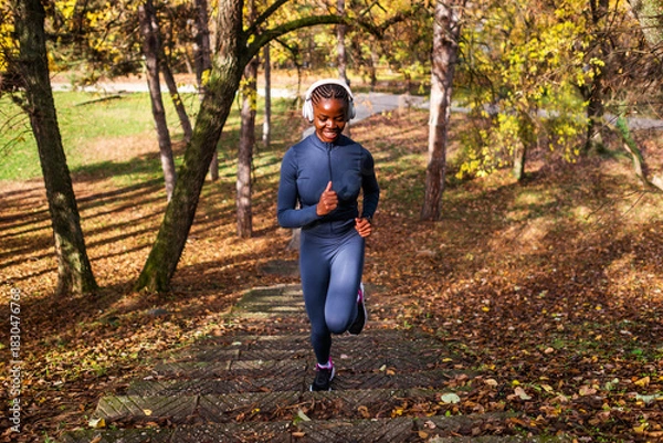 Fototapeta Amid warm autumn tones, a runner makes her way up a path lined with trees, appearing energized and happy during her outdoor workout.