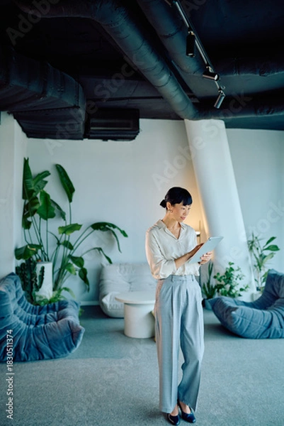 Obraz Businesswoman standing, working with a tablet in a contemporary office lounge, combining professional technology with a green interior