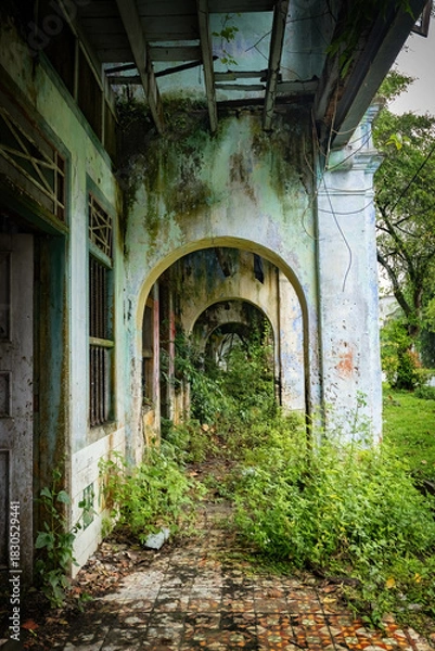 Fototapeta Weathered colonialera corridor in Papan Heritage Village, with peeling paint, overgrown plants, and an old rattan chair adding to the abandoned yet atmospheric charm of this historic Malaysian