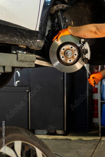 Fototapeta Mechanic with orange gloves using a wrench on the brake disc. Vehicle repair and safety maintenance in the workshop.