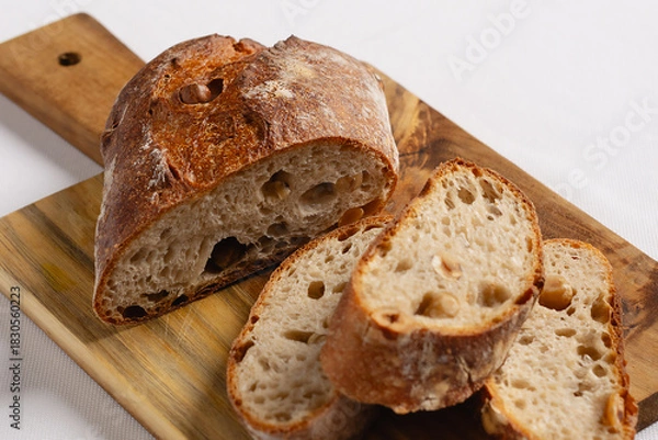 Fototapeta Sliced artisanal sourdough bread with hazelnuts on a cutting board. Rustic baked product for breakfast or snack.