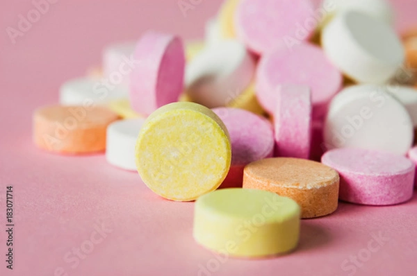 Fototapeta Close up of pile of chewable antacid acid indigestion relief tablets with fruit flavour in pastel colors, such as pink, yellow, orange and white on light pastel pink background