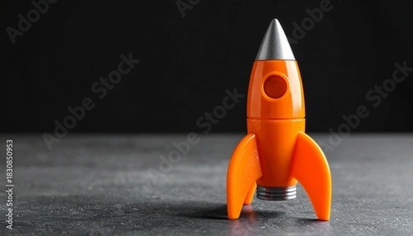 Obraz Orange Toy Rocket Standing Upright on Dark Surface with Black Background