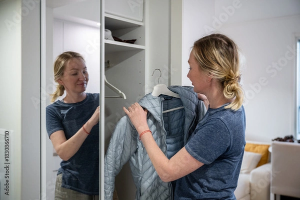 Obraz Woman putting on blue jacket in home wardrobe