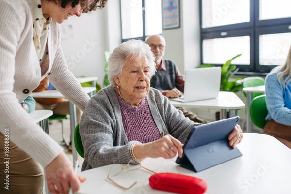 Fototapeta Elderly woman learning digital skills with tutor help.