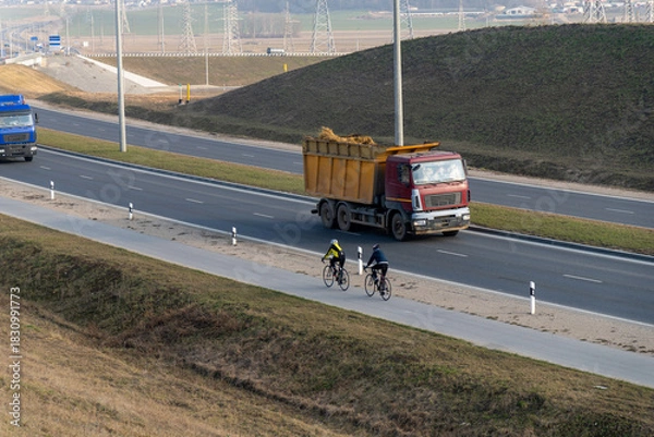 Obraz Two cyclists ride their bikes on a road parallel to a highway