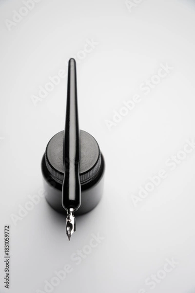 Obraz black ink bottle and a fountain pen resting on it, against a white background. Vertical photography, an aesthetic photo of old tools with a modern design