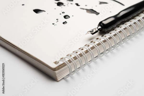 Obraz white spiral notebook with ink stains on the page and a black modern fountain pen. A stationery advertising background