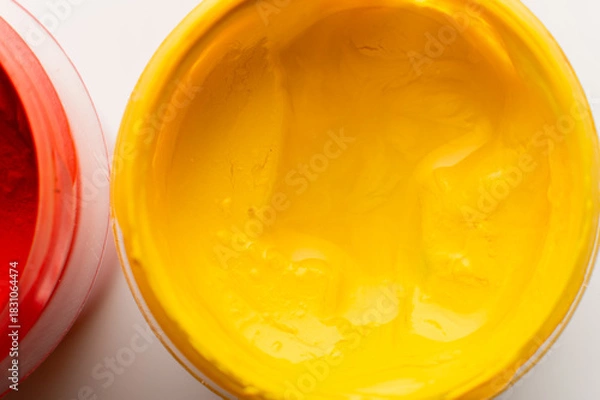 Obraz close-up shot of thick, bright yellow paint in a plastic jar. Gouache paint set. Jars of gouache are painted on a white background