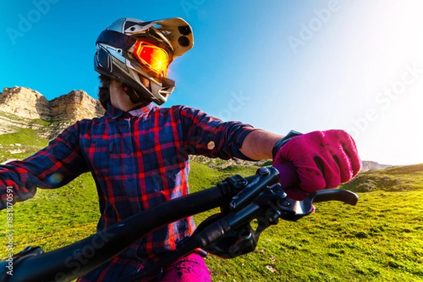 Obraz man on a mountain bike trains in the beautiful mountains. A wide-angle front view of the handlebars and the rider's hands, wearing a protective helmet