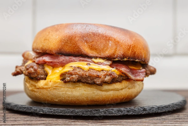 Fototapeta Smash burger au steak, bacon et fromage cheddar sur une ardoise, gros plan
