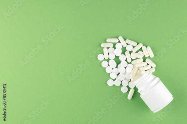 Fototapeta Close up white pill bottle with spilled out pills and capsules on pistachio green background with copy space. Focus on foreground, soft bokeh. Pharmacy drugstore concept. Top view