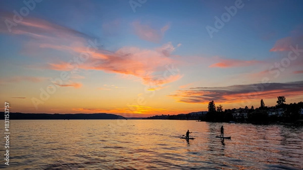Obraz Silhouettes of two people on Stand Up Paddle Board. Sunset on the lake Constance. Water sports.