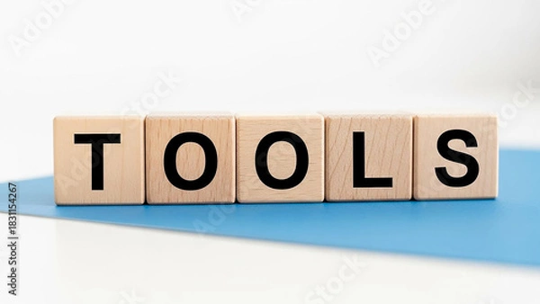 Fototapeta Wooden blocks spelling out the word tools on a blue surface against a white background in a studio shot