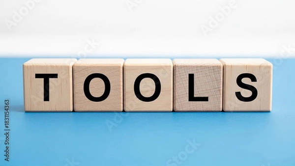 Fototapeta Wooden blocks spelling tools on a blue surface with a white background in a studio setting