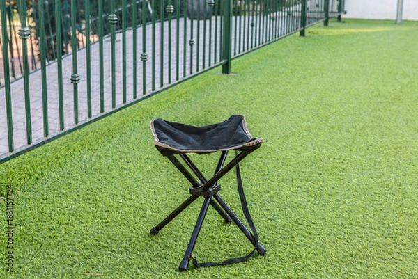 Fototapeta Outdoor folding chair positioned on green artificial grass near a fence