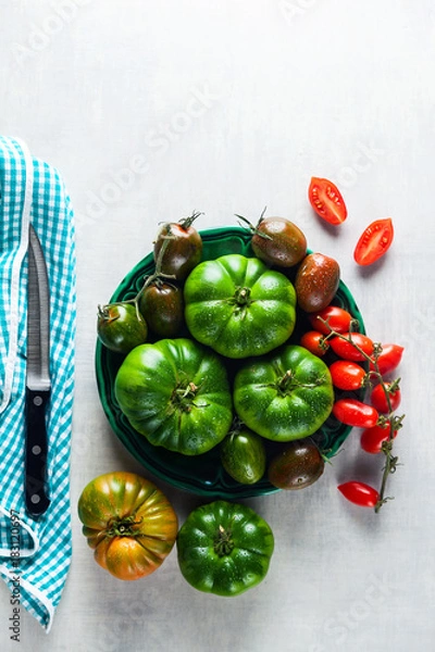 Fototapeta ingredients for salad from different types of tomato on a white stone table. cutting board, olive oil and condiments. healthy food, summer or spring menu