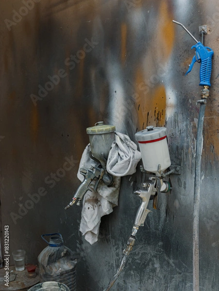 Fototapeta A spray gun hangs from a wall, covered in paint splatters, with paint buckets nearby. Concept of creative process, artistic work or industrial maintenance.