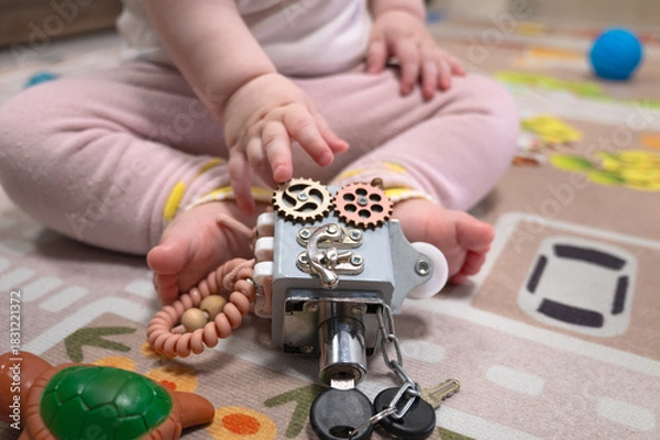 Fototapeta Toddler hands hold a vintage mechanical lock with chains and gears against a colorful rug. Concept of curiosity, exploration, and learning through play and discovery.