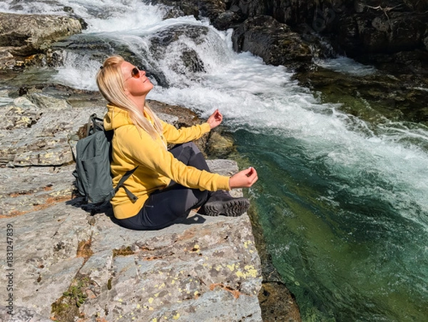 Fototapeta Blonde Woman Meditates by a Rushing Waterfall and Emerald River in the Pristine Norwegian Wilderness, Embracing Nature and Tranquility.