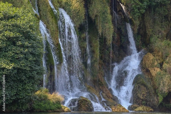 Obraz A peaceful waterfall cascading over moss-covered rocks surrounded by dense greenery, creating a refreshing and serene natural landscape.
