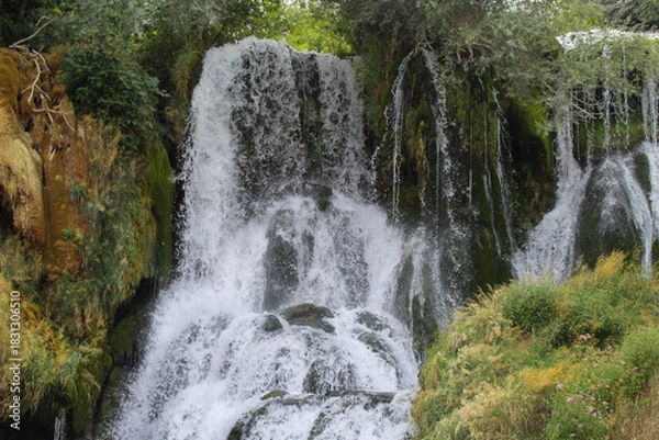 Obraz A dramatic natural waterfall crashing over moss-covered rocks, highlighting the raw power and beauty of untouched nature.